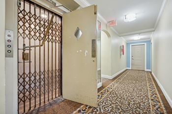 A hallway with a patterned carpet and a door with a metal grate.